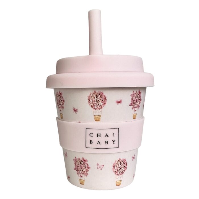 A babyccino cup with butterflies and air balloons with a pale pink background and a silicone lidded band and matching straw