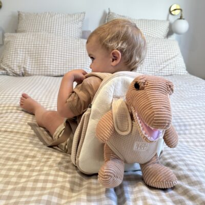 child with beige backpack on with harness and plush dinosaur soft toy